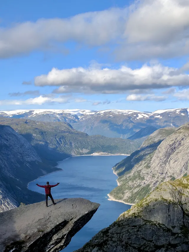 Seph standing on a cliff edge above a fjord, arms raised